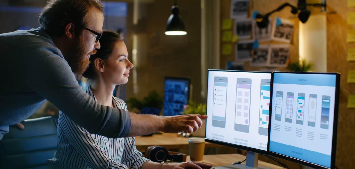 Eine Kollegin zeigt auf dem Bildschirm ihres Notebooks eine Anwendung. Diese App hat sie entwickeln lassen.