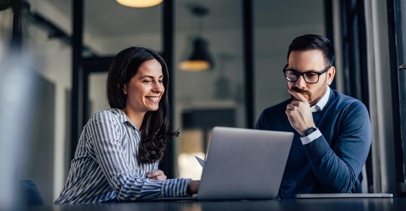 Ein heller Konferenzraum mit zwei Personen vor einem Notebook. Beide besprechen die Auswahl eines App-Entwicklung-Dienstleisters und prüfen Angebote.