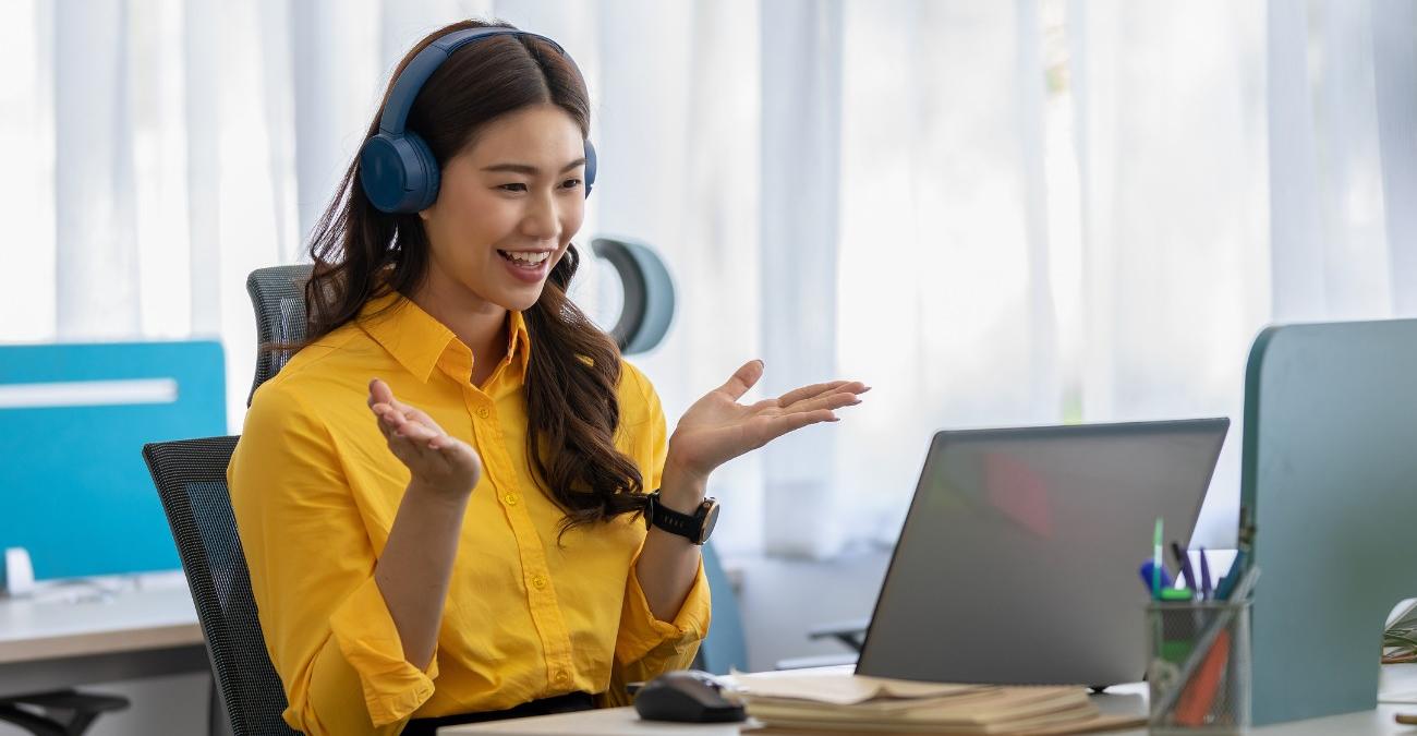 Eine junge Angestellt sitz im hellen Büro. Sie gestikuliert gut gelaunt vor ihrem Notebook. Dabei probiert sie die neue Authetifizierung in Unternehmenssoftware aus.