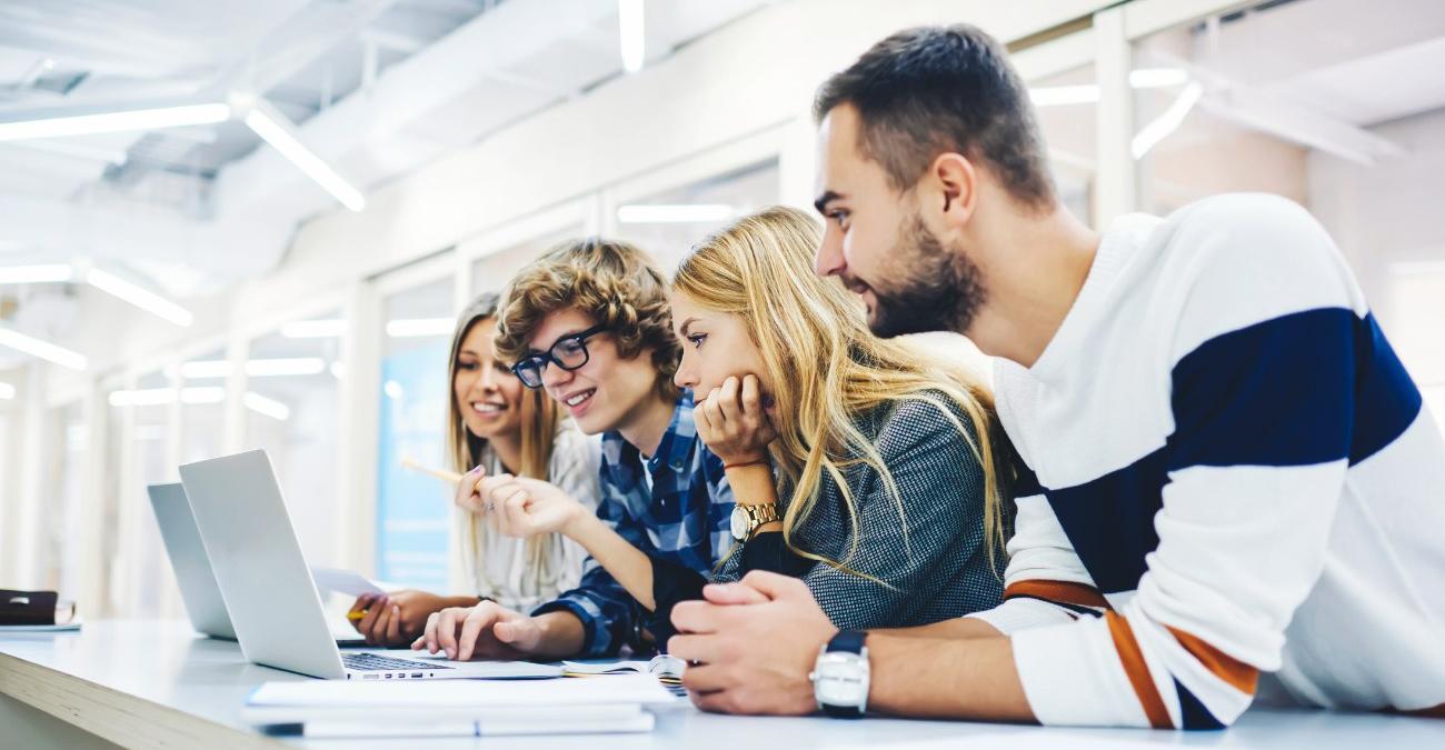 Vier Kolleginnen und Kollegen blicken gemeinsam auf einen Laptop-Bildschirm in einem modernen Büro, ein Symbolbild für Barrierefreiheit bei Legacy-Modernisierung, wenn ein Team ein bestehendes System gemeinsam prüft und schrittweise zugänglicher gestaltet.