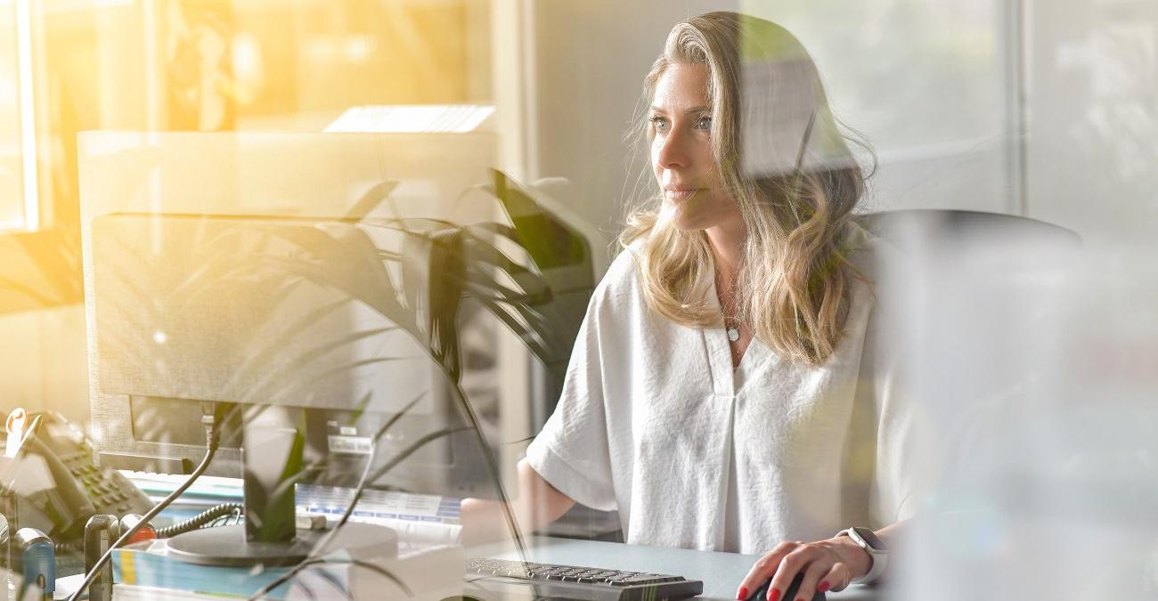 Eine Geschäftsfrau arbeitet durch eine Glasscheibe gesehen konzentriert an ihrem Schreibtisch, ein Sinnbild für die strukturierte Steuerung des Notfallmanagements mit einer BCM Software.