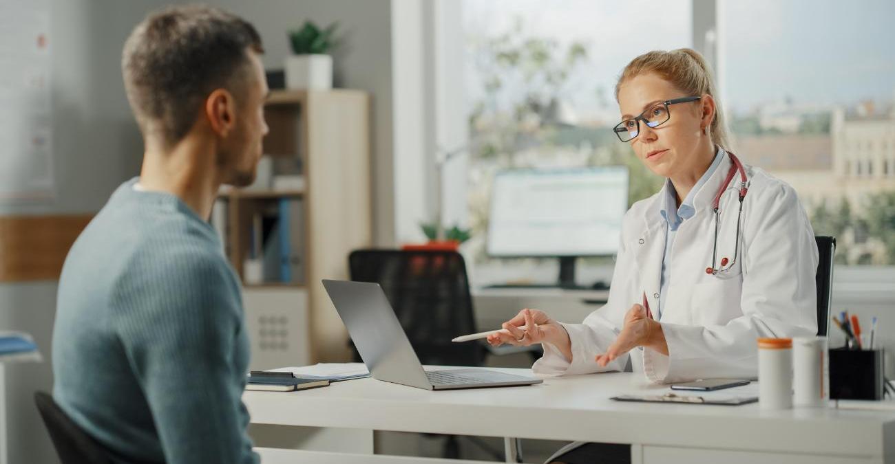 Eine Ärztin sitzt vor ihrem Patienten am PC. Sie arbeitet mit einer Branchenlösung für das Gesundheitswesen.