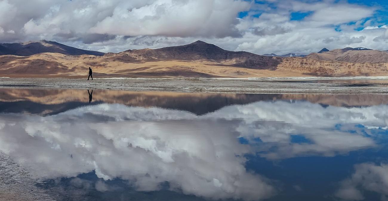 Einzelne Person geht am Ufer eines spiegelglatten Bergsees entlang, in dem sich der wolkenverhangene Himmel spiegelt – symbolisches Titelbild zum Thema Cloud Middleware