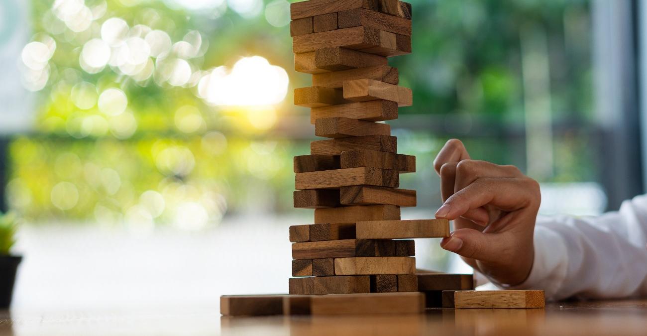 Hand entnimmt vorsichtig einen Baustein aus einem Holzturm, Symbolbild für die Risikoabwägung bei CMDB und Change Management.