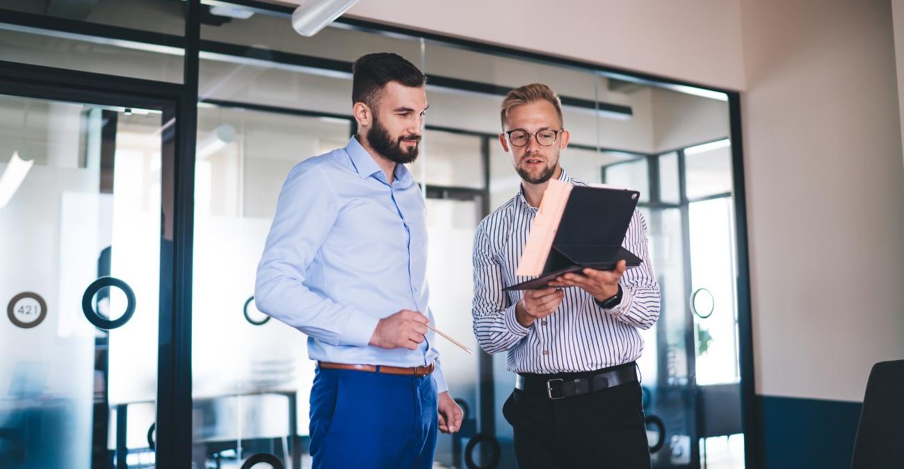 Zwei Berater besprechen Data Lifecycle Management sitzend vor einem Tablet in einem modernen Büro inklusive Planung von Datenstrategie und strukturiertem Datenlebenszyklus.