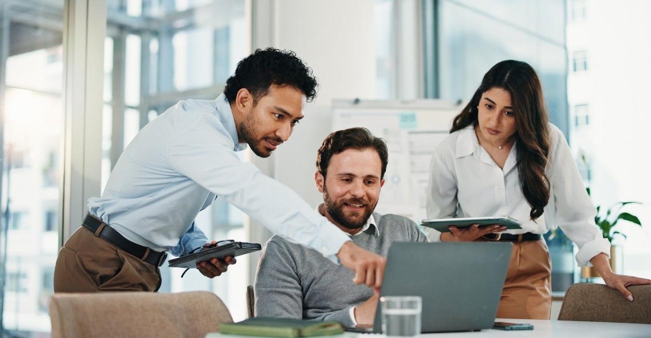Ein kleines Team sitzt im Büro gemeinsam an einem Laptop und zeigt auf den Bildschirm, um Daten und Abläufe zu besprechen – Sinnbild für die Datensicherung für kleine Unternehmen ohne eigene IT-Abteilung.