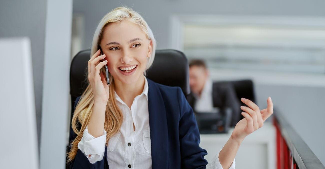 Eine junge, dynamische Angestellte im Großraumbüro eines Konzerns telefoniert gut gelaunt mit einem Kunden. Dank Enterprise Application Integration hat sie die wichtigsten Daten auf ihrem Handy stets im Blick.