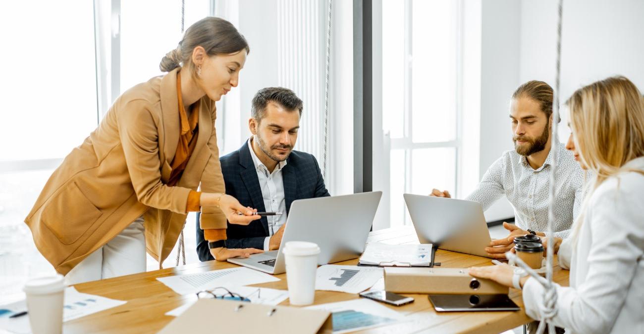  Eine Gruppe junger Büroangestellter sitzt in legerer Geschäftskleidung an einem Besprechungstisch im hellen Büro und plant gemeinsam die Übergabe-Workshops für einen anstehenden EVB-IT-Anbieterwechsel.