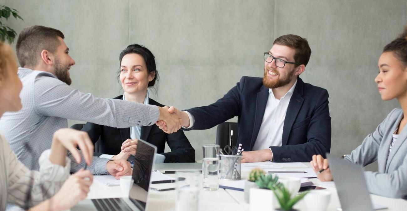 Vorgesetzter und Mitarbeiter geben sich im Meeting die Hand – Sinnbild für die vertragliche Einigung bei einem EVB-IT-Vertrag für Softwarepflege.