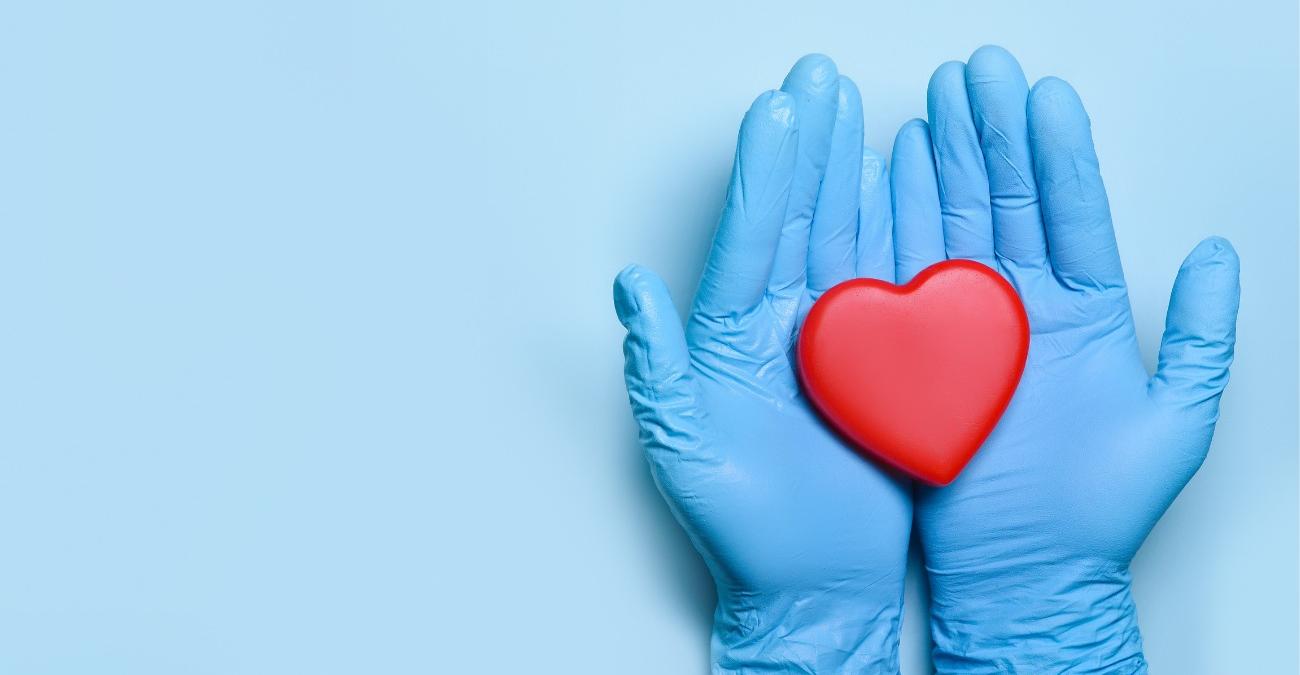 Zwei behandschuhte Hände eines Arztes halten ein rotes Herz – Sinnbild für die Behandlung und Versorgung von Patienten, die ein verlässliches Health IT Service Management im Hintergrund am Laufen hält.