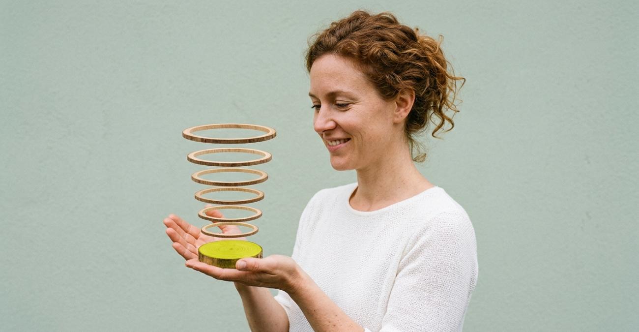 Eine lächelnde Frau hält eine gelbgrüne Holzscheibe in der Hand, darüber schweben dünne Holzringe in exakter Ordnung, ein Sinnbild für das inkrementelle Backup, bei dem jede Sicherung nur den Zuwachs auf der Vollsicherung ergänzt.