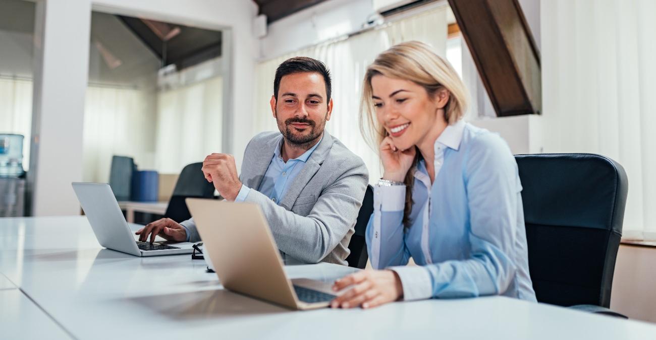 Zwei Verwaltungsmitarbeiter sitzen in einem hellen Konferenzraum an ihren Laptops und stimmen gemeinsam die nächsten Schritte zur IT für Kommunen ab.