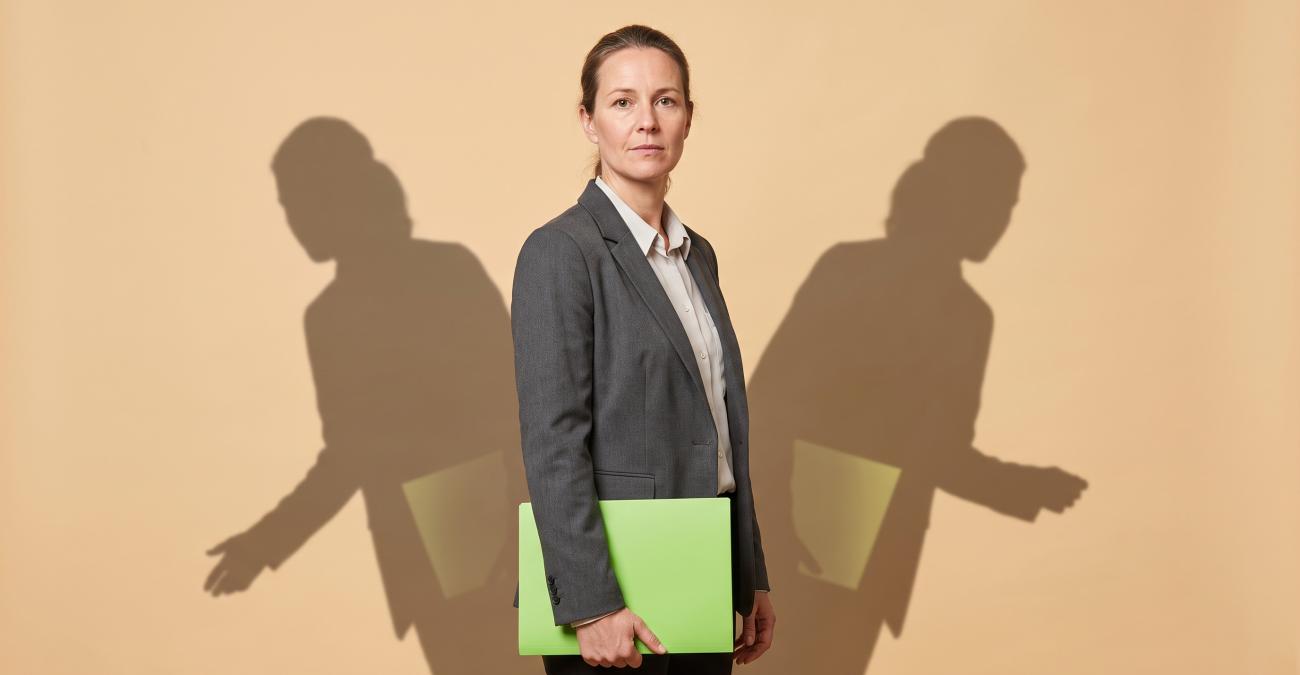 Eine Frau mit gelbgrüner Mappe wirft zwei Schatten in verschiedene Richtungen, die beide dieselbe Mappe tragen: Sinnbild für widersprüchliche Auskünfte in der IT-Infrastruktur-Verwaltung.