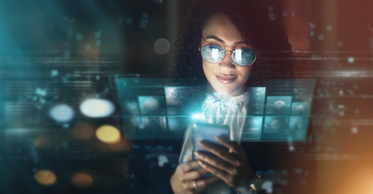 Im Vordergrund spiegeln sich futuristische Bildschirme. Eine junge Frau sitzt mit ihrem Handy in einem modernen Büro. Sie erkundigt sich nach einer KI-Integration für ihr Unternehmen. Der Hintergrund ist nur verschwommen zu erkennen.