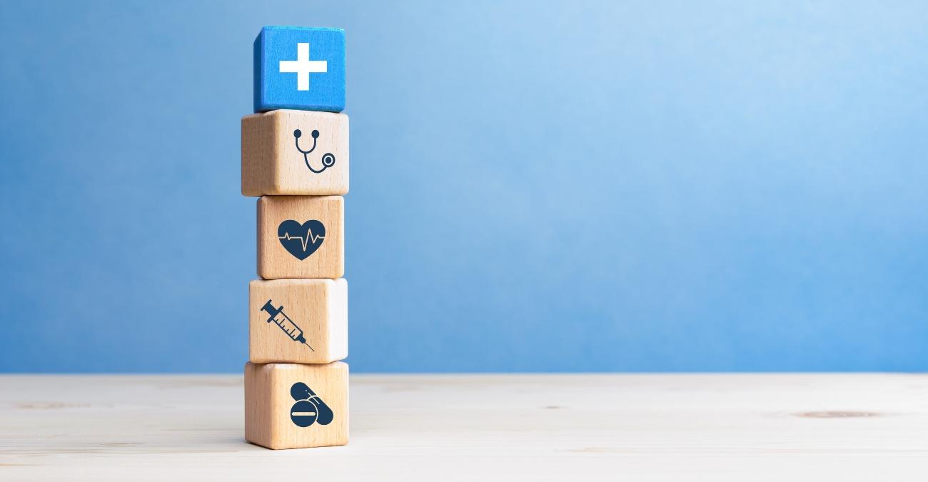 Hölzerne Blöcke mit medizinischen Symbolen vor einem hellblauen Hintergund stehen symbolisch für die Integration von KIM im Gesundheitswesen.