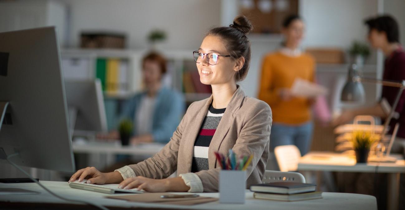 Eine junge Programmiererin sitzt in einem hellen Office an ihrem Notebook. Sie programmiert in Laravel.