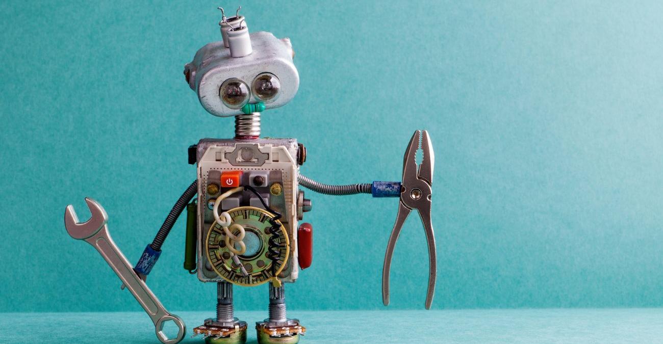 Himmelblauer Hintergrund. Im Vordergrund steht ein kleiner Roboter aus Ersatzteilen, der einen Schraubenschlüssel und eine Kneifzange hält. Ein Symbolbild für Laravel-Wartung.