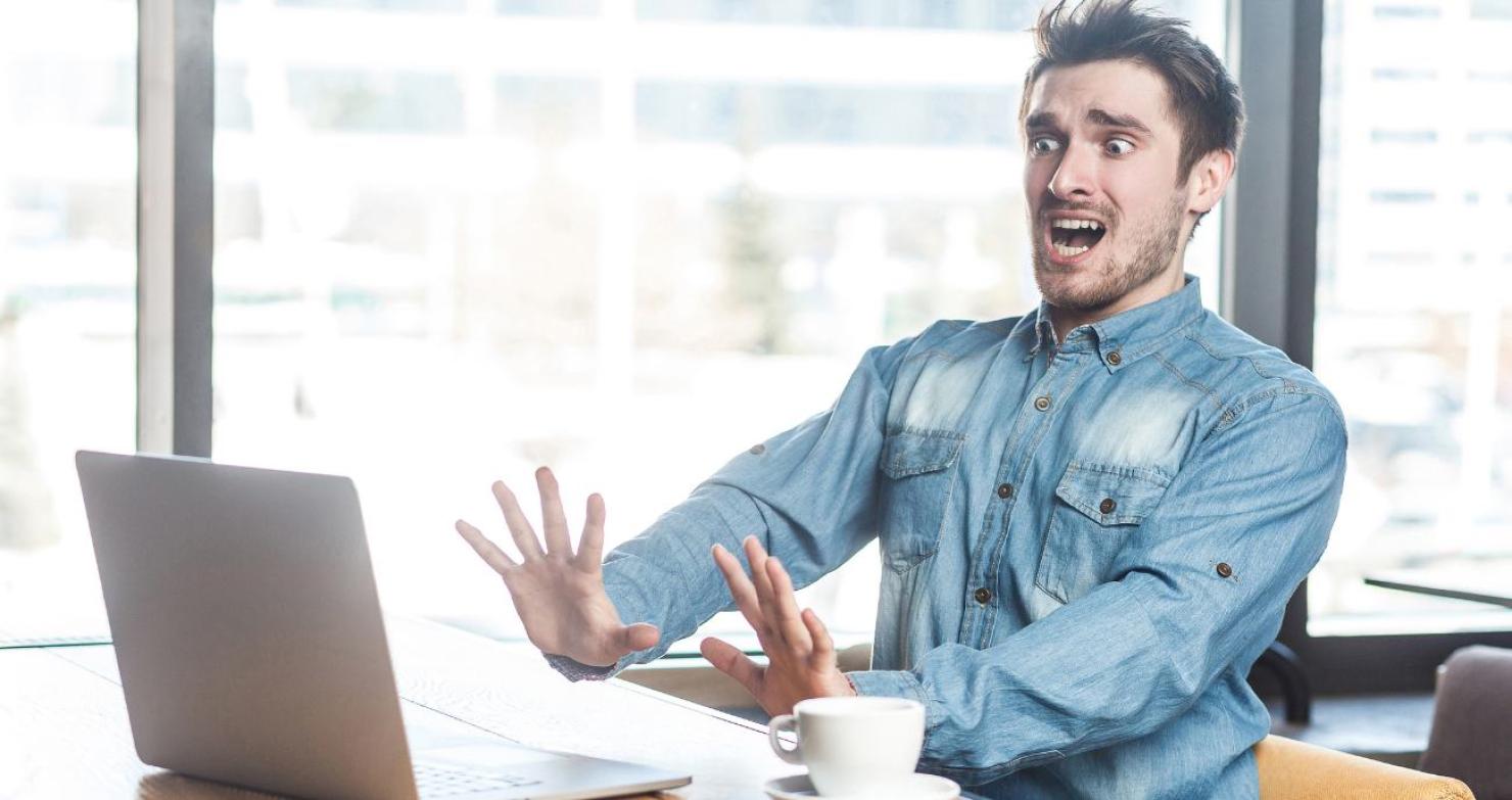 Ein Mann sitzt vor seinem Laptop mit entsetzter Geste und aufgerissenen Augen – Symbolbild für unerwartete IT-Kosten ohne strukturiertes Lifecycle Costing