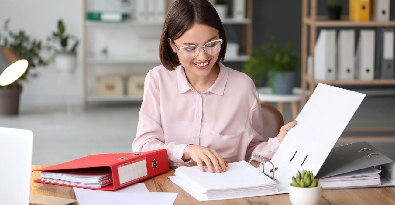 Eine junge Frau bearbeitet konzentriert Unterlagen an ihrem Schreibtisch im Büro – ein Sinnbild für strukturierte Maßnahmen zur Datensicherung in Verwaltung und Mittelstand.