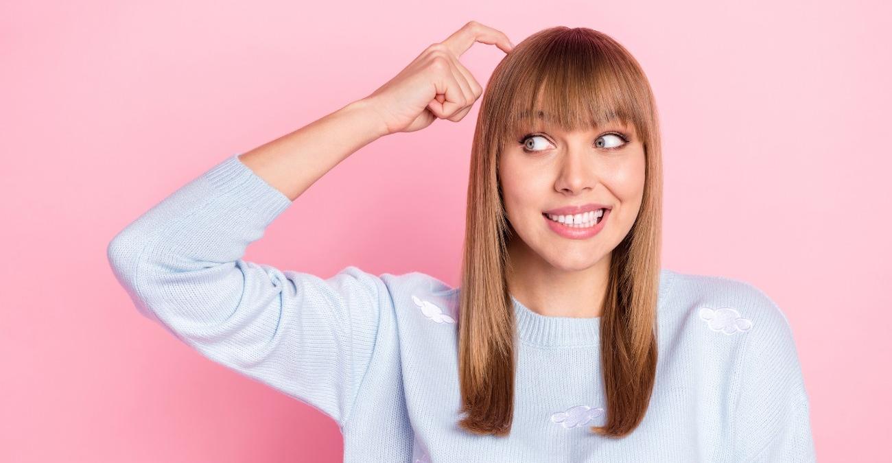 Eine junge Frau mit Pony und hellblauem Strickpullover steht vor rosa Hintergrund, blickt nachdenklich zur Seite und tippt sich grübelnd an den Kopf – als wäge sie ab, ob für ihr Projekt Middleware oder eine API die richtige Wahl ist.