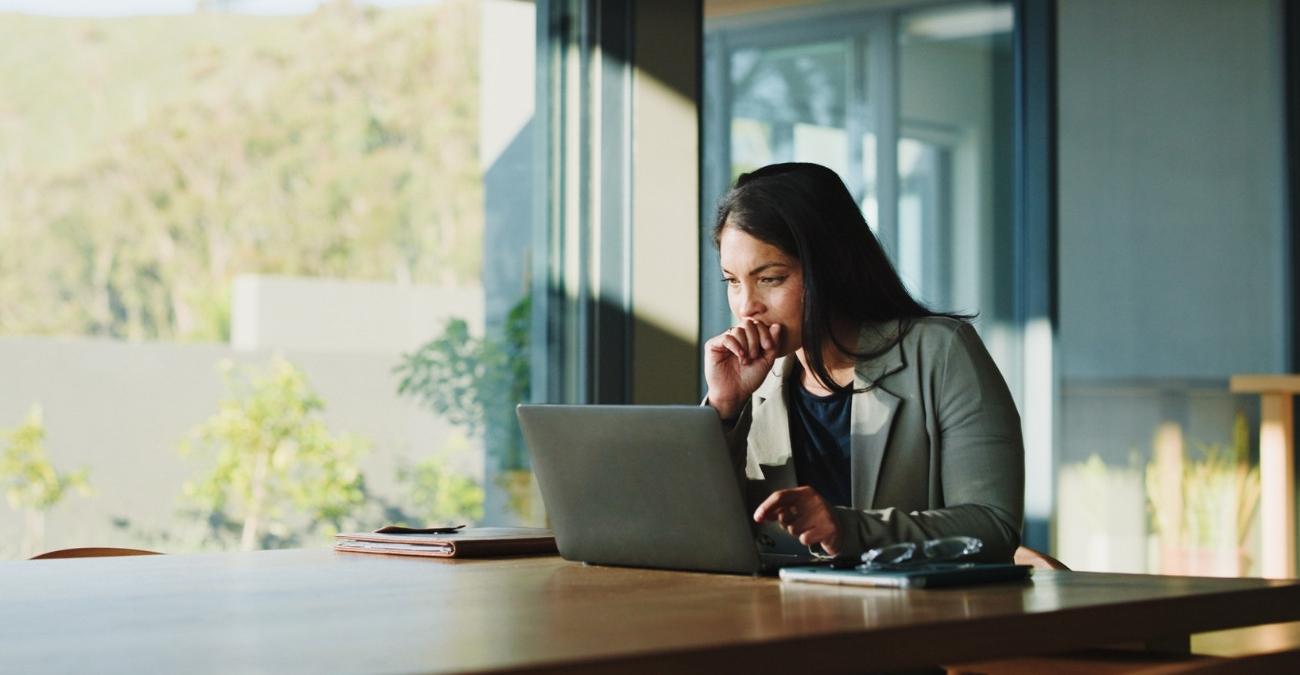 Eine Geschäftsführerin sitzt an einem großen Tisch im Büro. Sie sieht konzentriert auf den Bildschirm ihres Notebooks. Sie studiert das neue NIS-2 Umsetzungsgesetz.