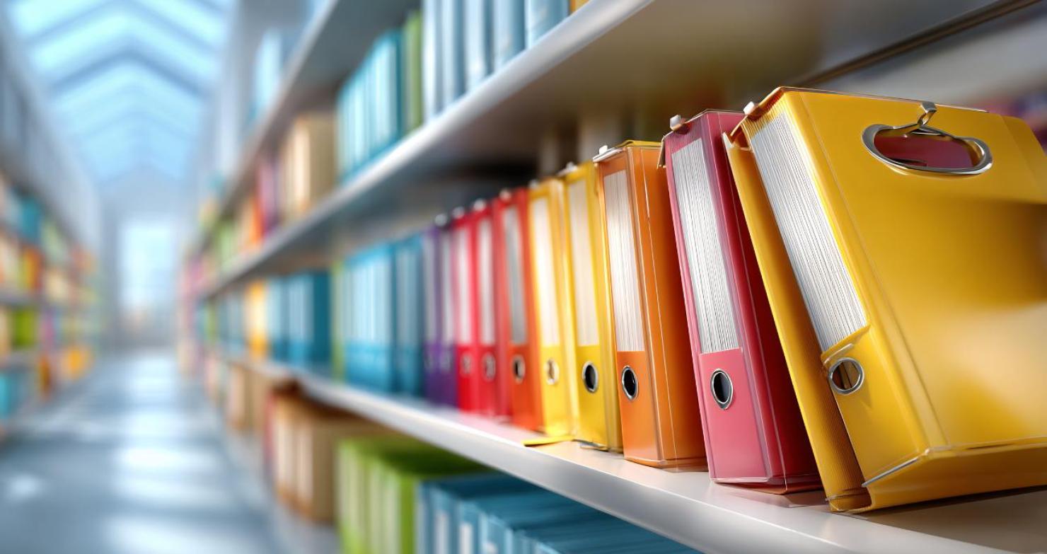 Wir sehen bunte Akten in einem großen weißen Regal. Ein Symbolbild für die Einführung von NIS2 in öffentlichen Verwaltungen.