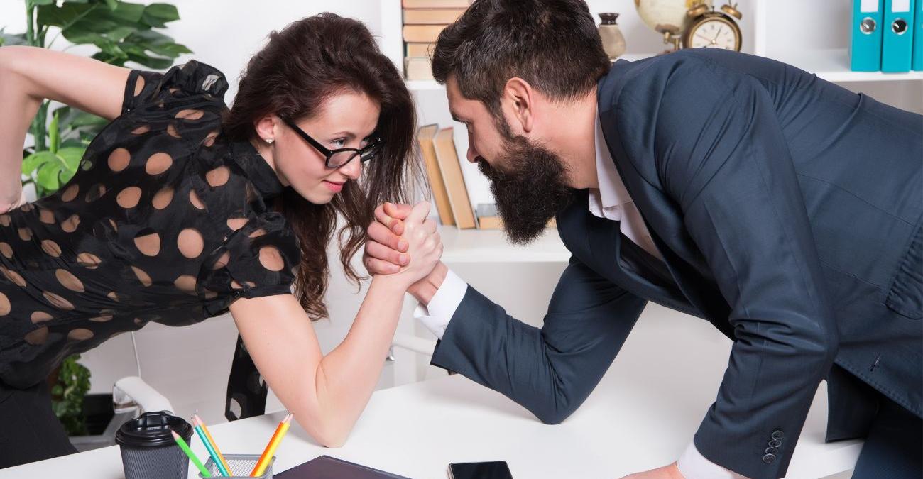 Ein Mann und eine Frau machen Armdrücken am Bürotisch. Ein Symbolbild für den PHP-Framework-Vergleich.