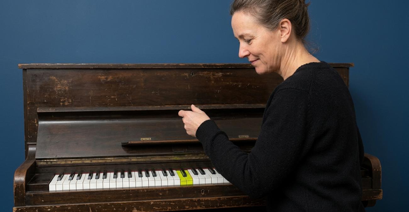 PHP-Entwicklung: vertrautes Gehäuse, erneuerte Mechanik Eine Frau öffnet den Deckel eines alten Klaviers und legt darunter eine fabrikneue Klaviatur frei. Sinnbild für PHP-Entwicklung auf einer Sprache mit erneuertem Kern.
