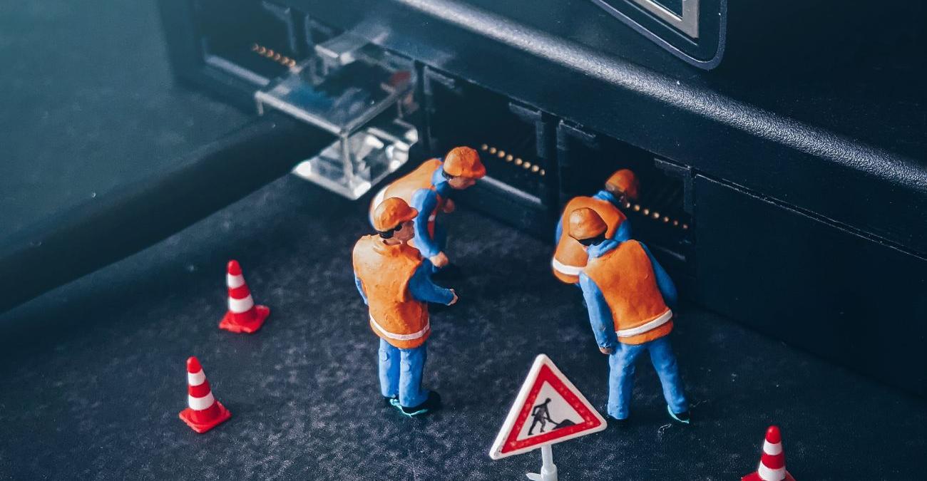 Klein Spielzeug-Bauarbeiter stehen vor einem PC-Desktop und begutachten die Anschlüsse. Ein Symbolbild für PHP-Wartung.