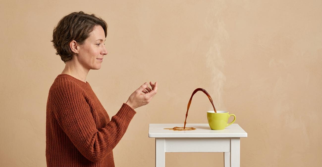 Verschütteter Kaffee fließt vom Tisch zurück in die Tasse, eine Frau sieht gelassen zu. Sinnbild für Point in Time Recovery nach einem Fehler.