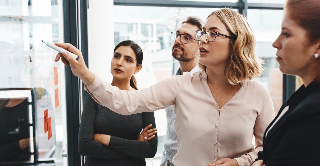 Ein heller Konferenzraum. Mehrere Personen stehen für einem Whiteboard und diskutieren konzentriert über ein Schwachstellenmanagement-Konzept.