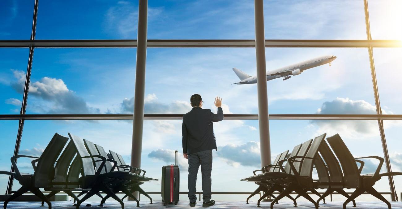 Ein junger Geschäftsmann winkt am Flughafen zum Abschied dem startenden Flugzeug hinterher — ein Symbolbild für die geordnete Verabschiedung von Altsystemen bei der Software-Ablösung in KRITIS-Betrieben.