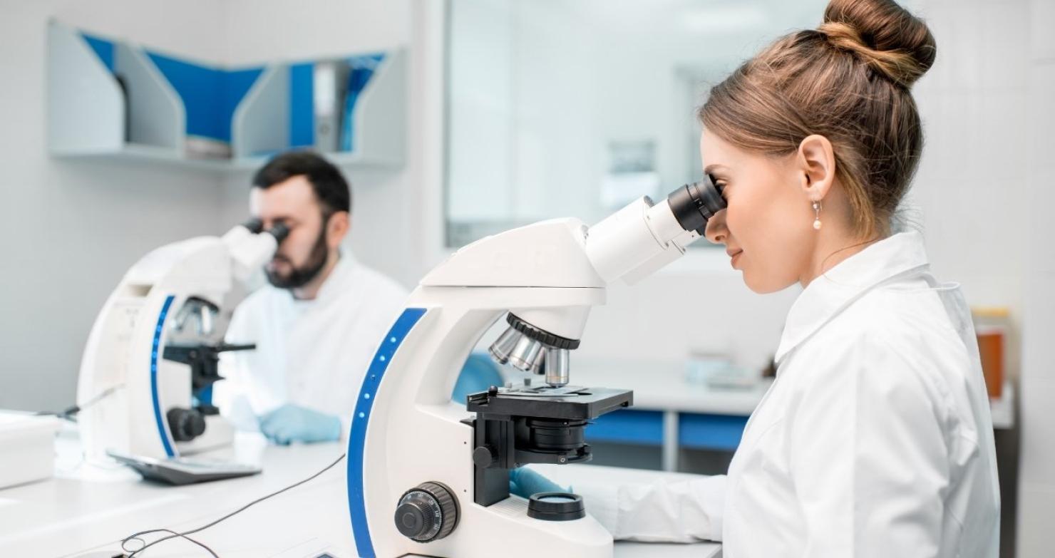 Zwei Forschungsmitarbeitende in weißen Kitteln sitzen an hochmodernen Mikroskopen und werten konzentriert Proben aus. Ein Sinnbild für die wissenschaftliche Auswertung von Satellitendaten in der Erdbeobachtung.