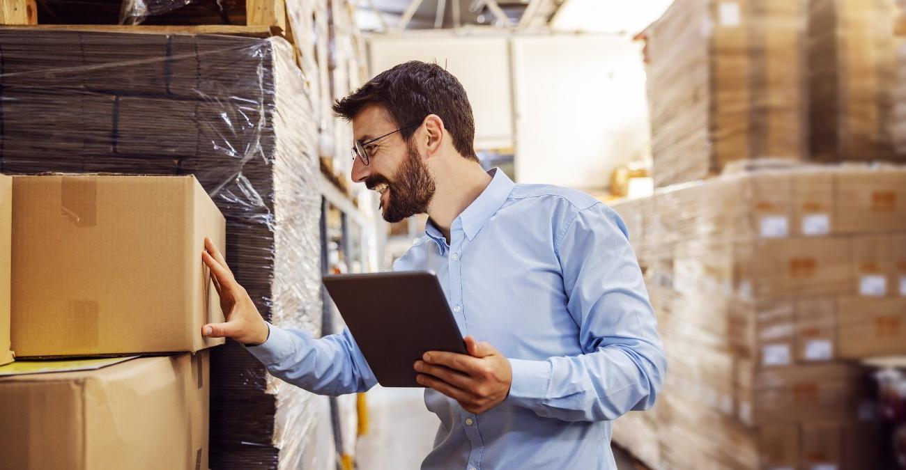 Ein Mitarbeiter prüft mit einem Tablet Kartons und Paletten im Lagergang, ein Symbolbild für den Einsatz von Software für Logistikdienstleister.