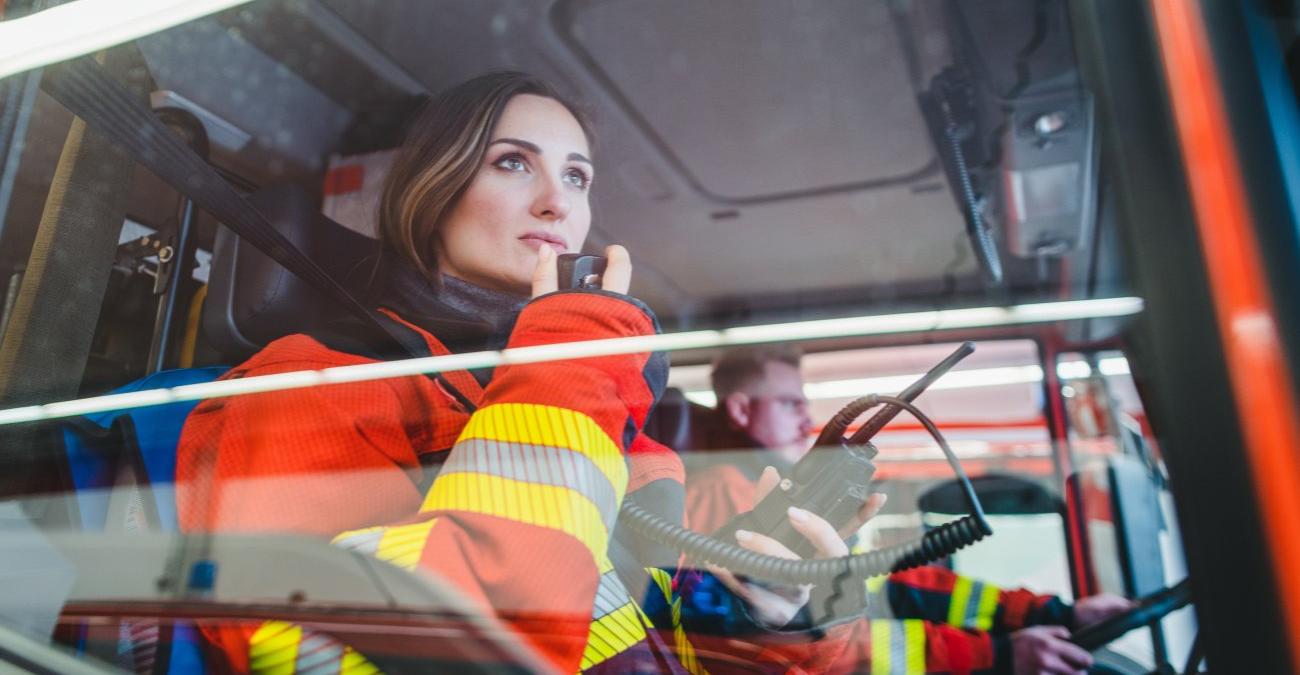 Eine Feuerwehrfrau sitzt im Einsatzwagen mit einem Funkgerät. Ein Symbolbild für Softwareentwicklung für das KRITIS-Umfeld.
