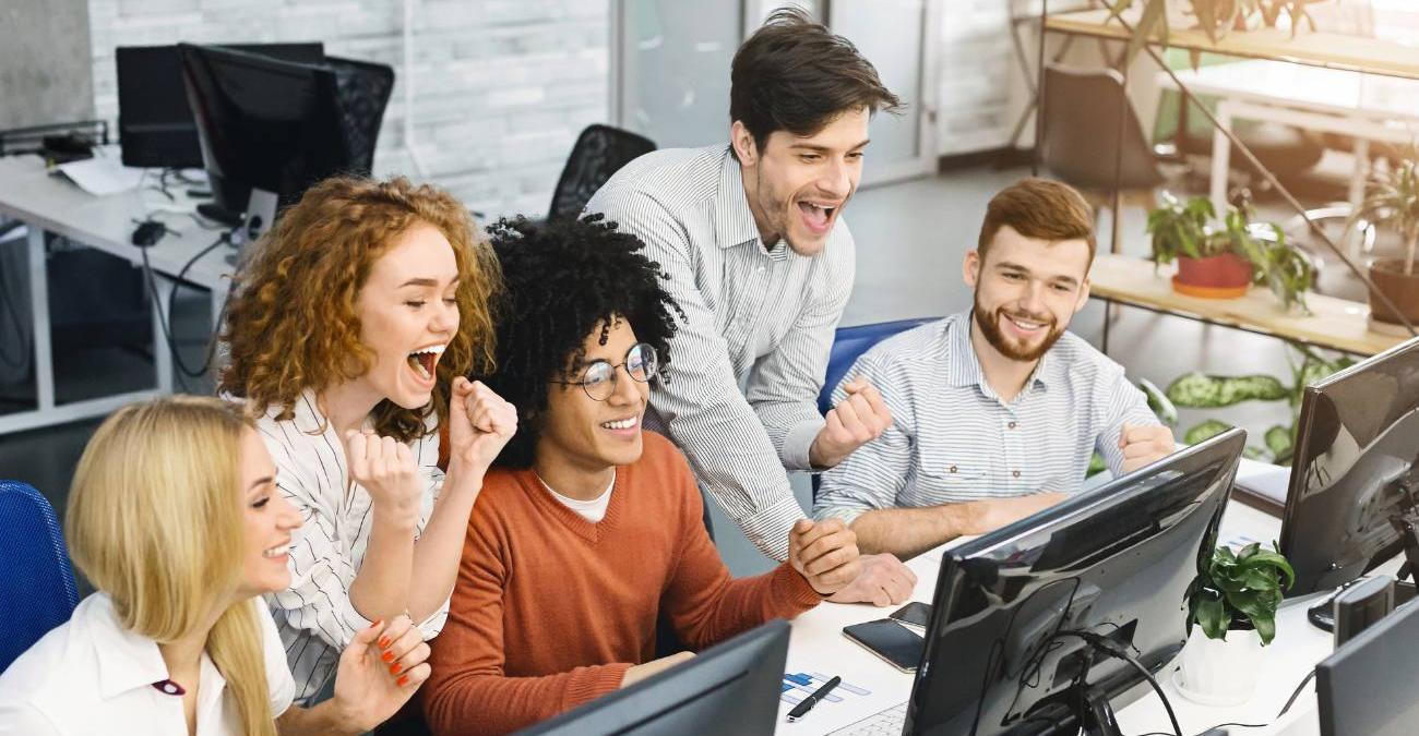 Ein Agenturloft. Die jungen, dynamischen Mitarbeiter und Mitarbeiterinnen der Symfony-Agentur sitzen und stehen um PC-Bildschirme herum und jubeln.