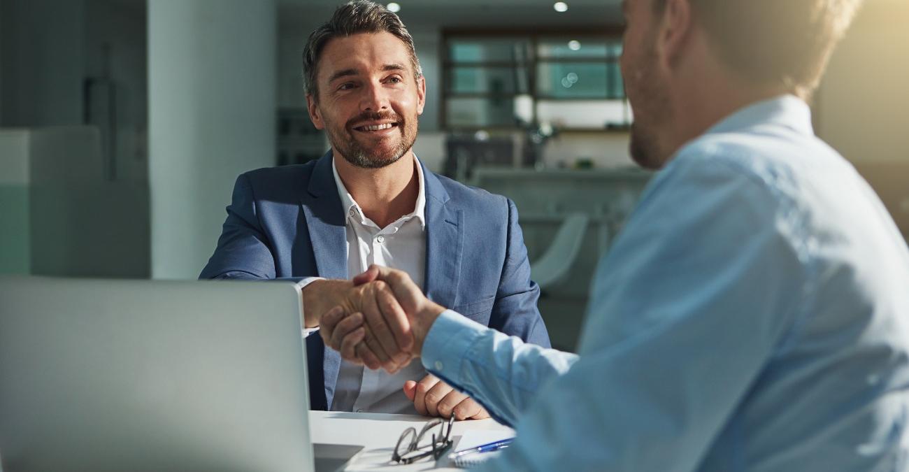 Zwei Geschätfsleute sitzen vor einem Notebook und schütteln sich die Hände. Sie haben gerade einen Wartungsvertrag für Individualsoftware unterschrieben.