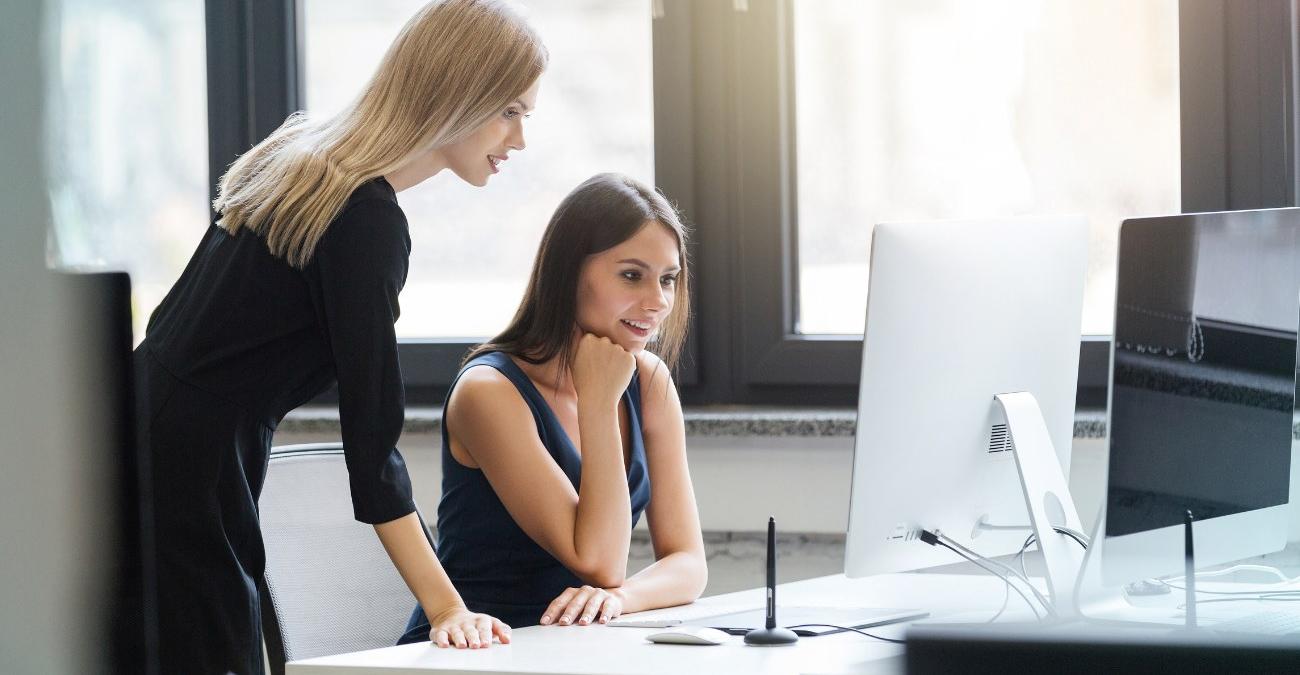 Zwei Mitarbeiterinnen einer Behörde sitzen im Büro und sehen fasziniert auf einen Computerbildschirm. Sie bestanen den Rollout der neuen WebApp, die nach der BITV-2.0-Checkliste für Fachverfahren designt wurde.