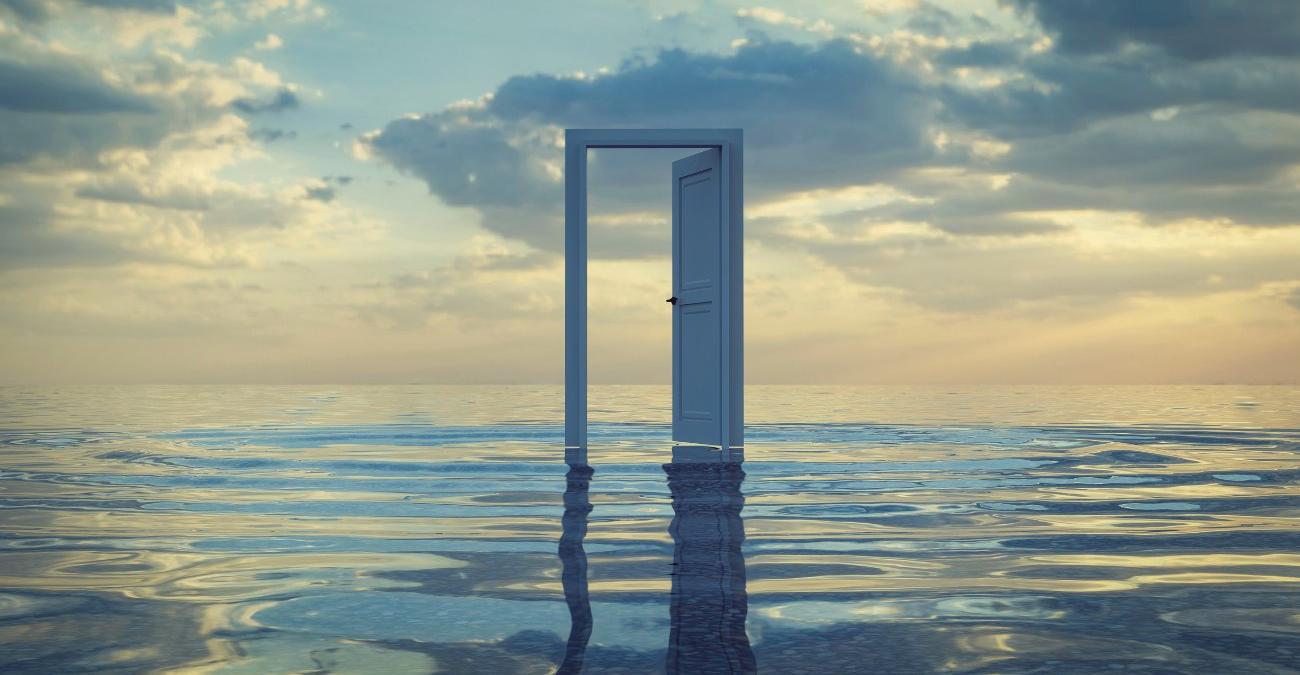 Dicke weiße Wolken am Himmel und ein zartes Abendrot. Eine weiße Tür steht inmitten eines Meeres auf den Wellen. Sie ist geöffnet. Symbolisch für Accessibility steht dieses Bild für WCAG-Konformität.