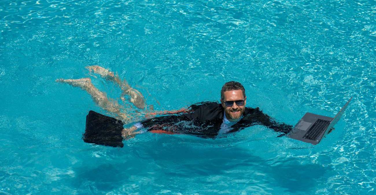 Ein Mann im Anzug schwimmt im Pool. In der einen Hand hält er seinen Aktenkoffer, in der anderen sein Notebook. Ein Symbolbild für Workflow Management Software in der öffentlichen Verwaltung.
