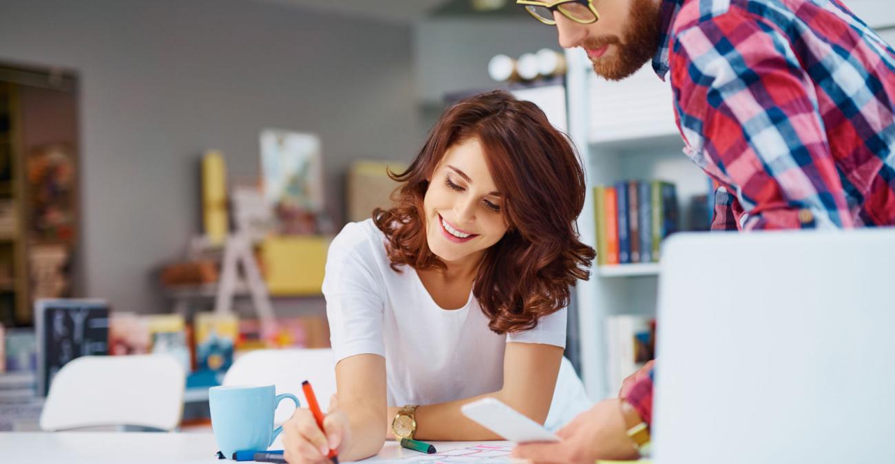 Zwei Mitarbeiter*innen einer Webagentur arbeiten mit Laptop, Zettel und Stift am Konzept einer Webseite.