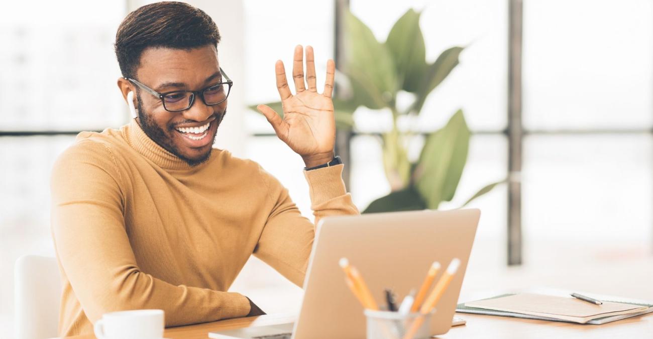 Arbeiten im Homeoffice während der Corona-Krise Ein Mitarbeiter sitzt an seinem Laptop und begrüßt winkend seine Kollegen in der Videokonferenz
