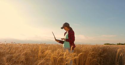 Eine Frau steht mit einem Laptop in einem Feld und betreibt klimaneutrale Webentwicklung.