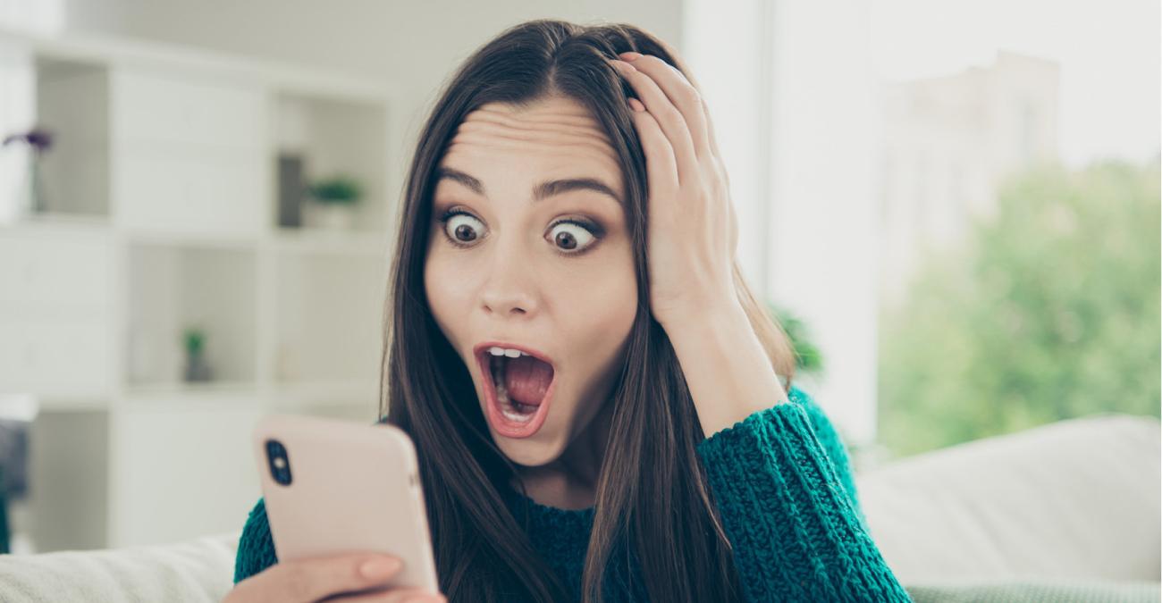 Frau schaut mit groĂen Augen auf ihr Smartphone Eine Frau schaut erstaunt auf ihr Smartphone.