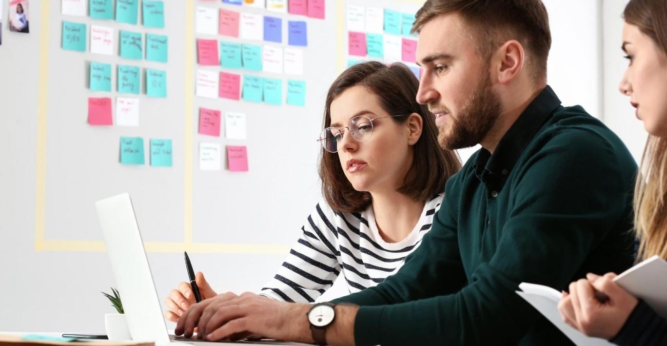 Ein Scrum Team bei der Sprint Planung mit Laptop und Zetteln an der Wand, die das weitere agile Vorgehen planen.