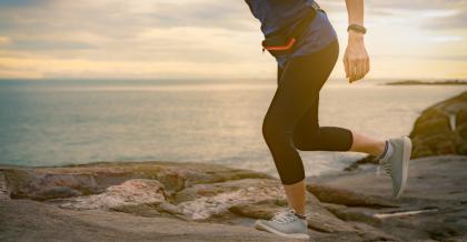 Eine Frau läuft in Turnschuhen und Laufkleidung einen Weg am Meer bei Sonnenuntergang entlang