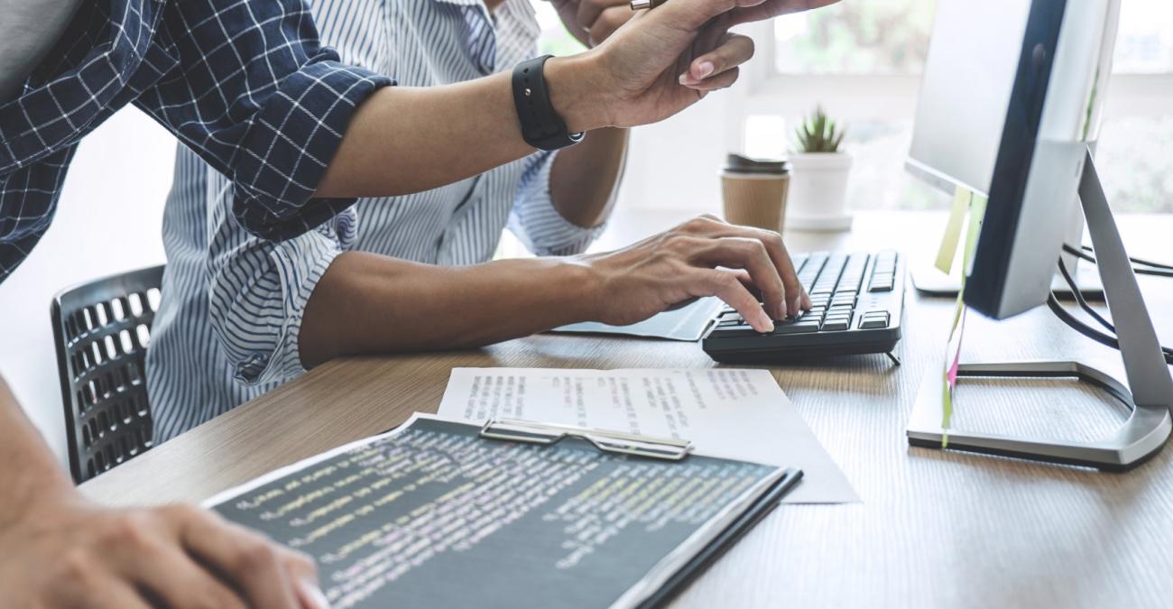 zwei Personen sitzen am Schreibtisch und arbeiten mit dem Computer