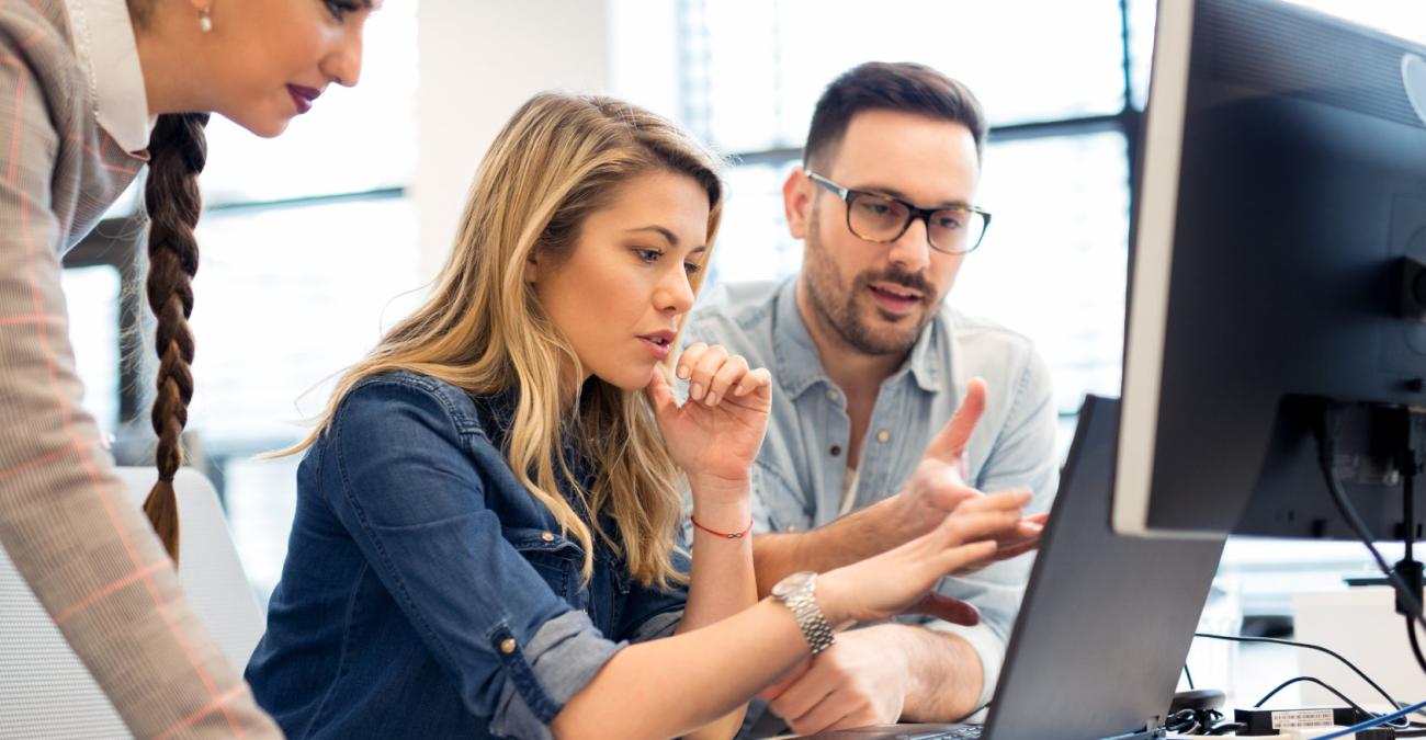 Zwei Frauen und ein Mann arbeiten zusammen an einem Computer