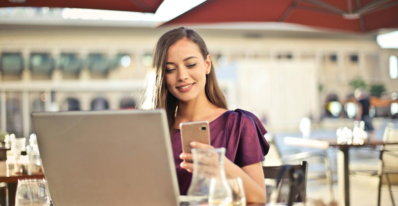 Frau sitzt im Café mit Laptop und Handy