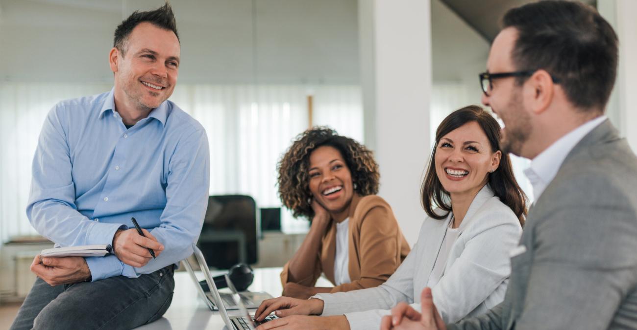 Vier Business Leute sitzen lachend vor einem Laptop am Schreibtisch